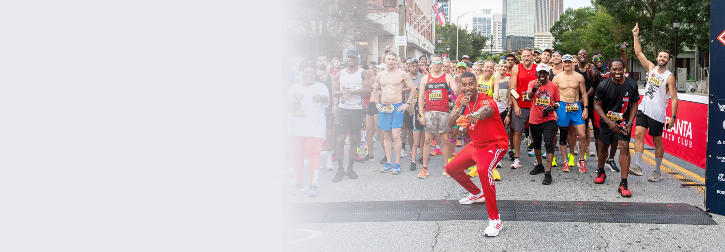 Diverse group of runners at the starting line of a race, with one man in red in front holding a microphone.