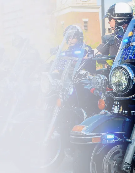 Police officers on motorcycles with flashing lights, one officer wearing a helmet and sunglasses.