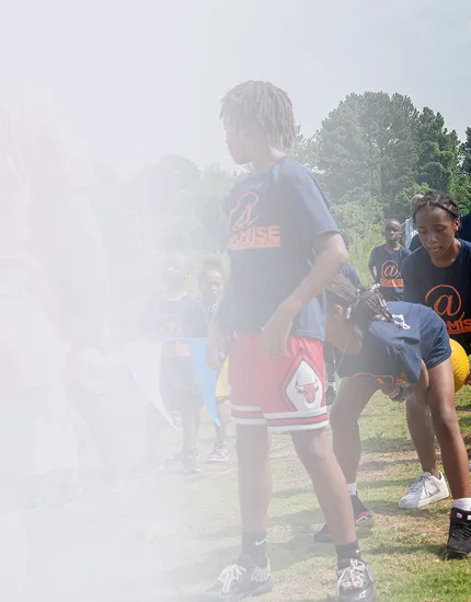 Children playing outdoors on grass, wearing matching navy blue T-shirts with an orange logo.