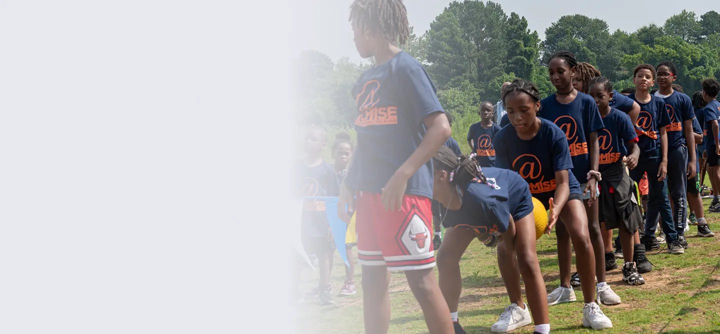 Group of children in matching navy blue shirts with orange 'Promise' logo playing outside on grass.