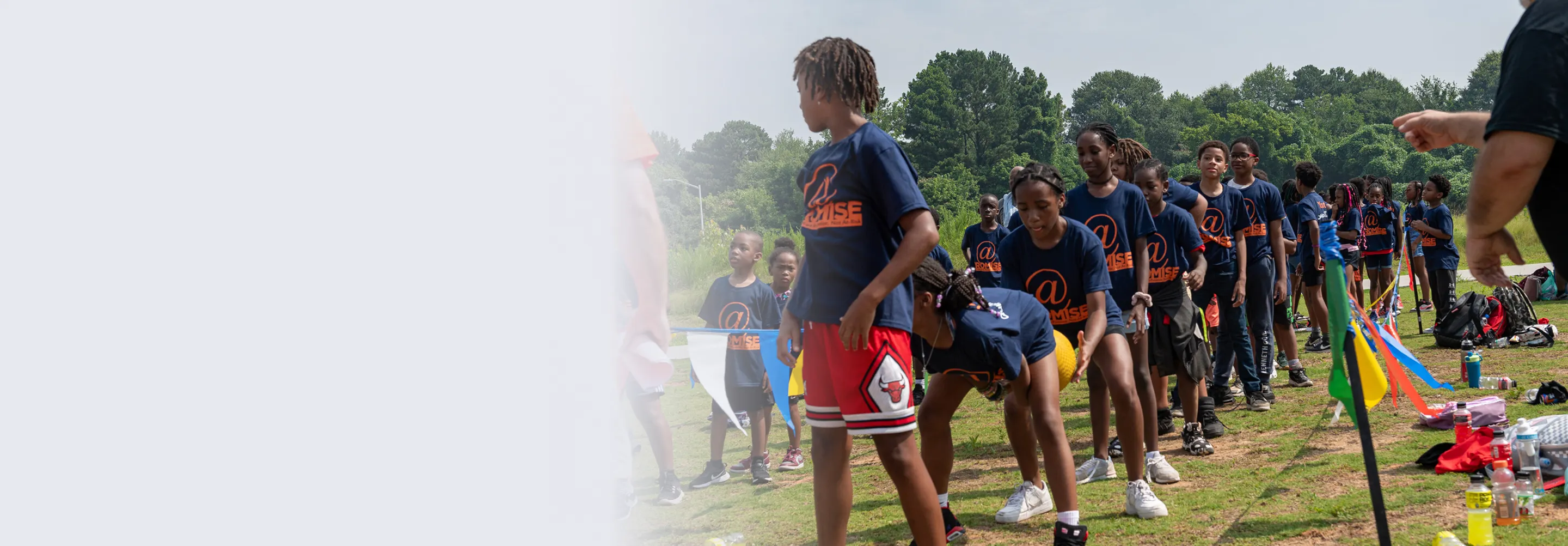 Group of children in matching navy blue event T-shirts lined up outdoors on grass with trees in background.