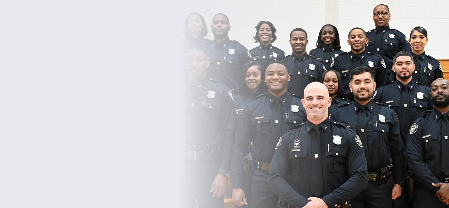 Three police officers standing together outdoors near a tree and a vehicle, smiling at the camera.