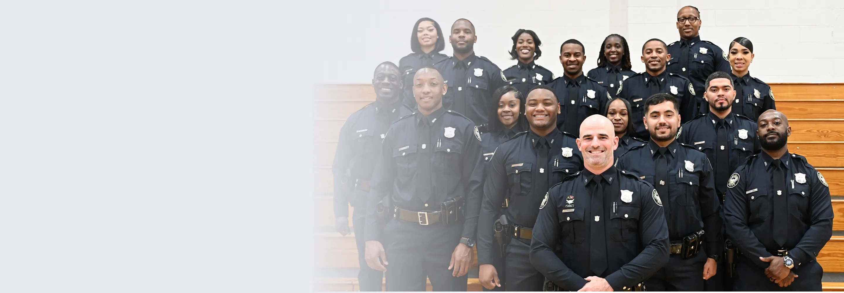 Four smiling police officers in uniform standing outdoors in front of a building and a tree.