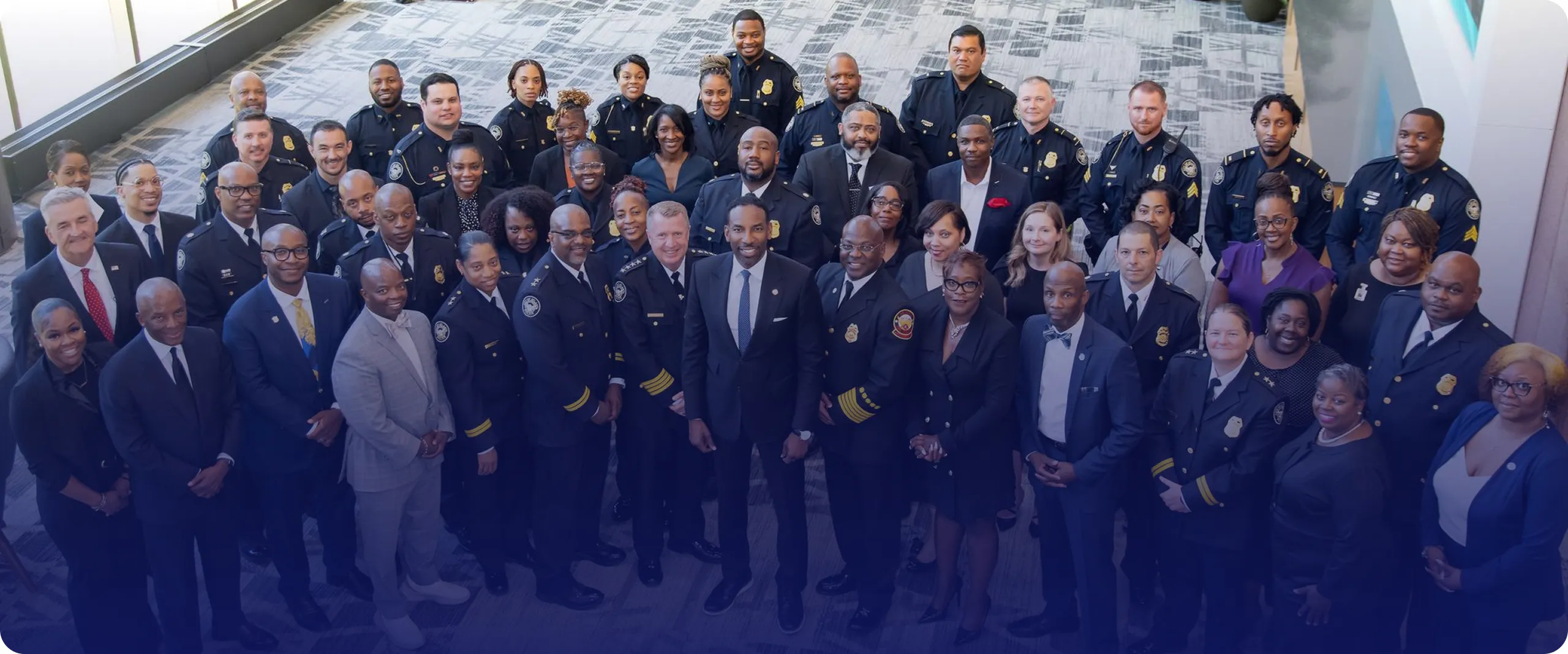 Group of diverse police officers and officials posing together indoors on a carpeted floor.