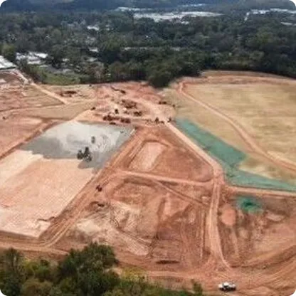 Aerial view of a large construction site with cleared land, dirt roads, and some construction vehicles amidst surrounding trees.