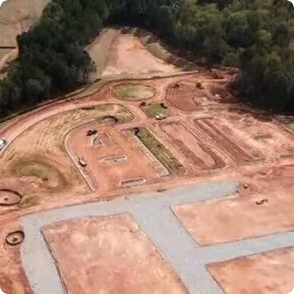 Aerial view of an off-road dirt track surrounded by trees, featuring winding paths and several vehicles.