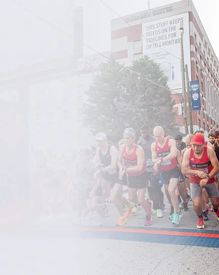 Group of runners in red and black athletic gear starting a race on a city street.