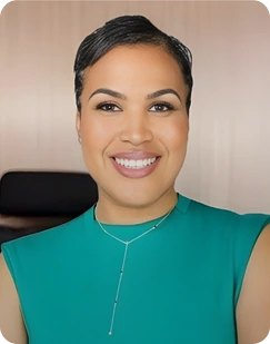Smiling woman with short styled hair wearing a teal sleeveless top and a delicate necklace.