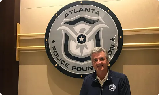 Man standing in front of a large circular Atlanta Police Foundation emblem on a wall.