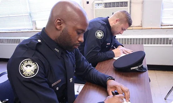 Two police officers in City of Atlanta uniforms sitting at a table and writing on paper.