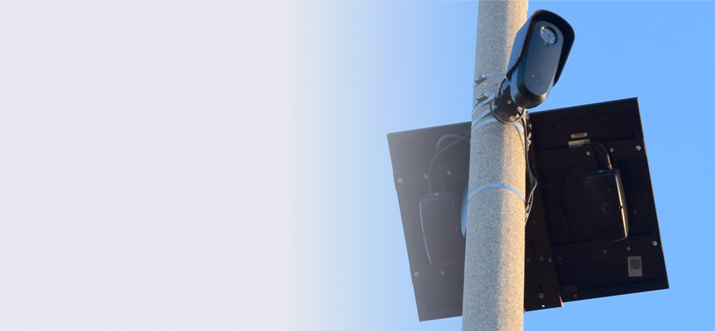 Surveillance camera mounted on a pole with a solar panel against a clear blue sky.