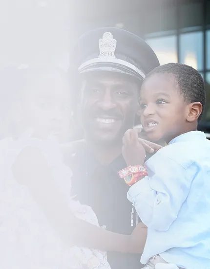 Smiling police officer holding a young boy wearing colorful bracelets.