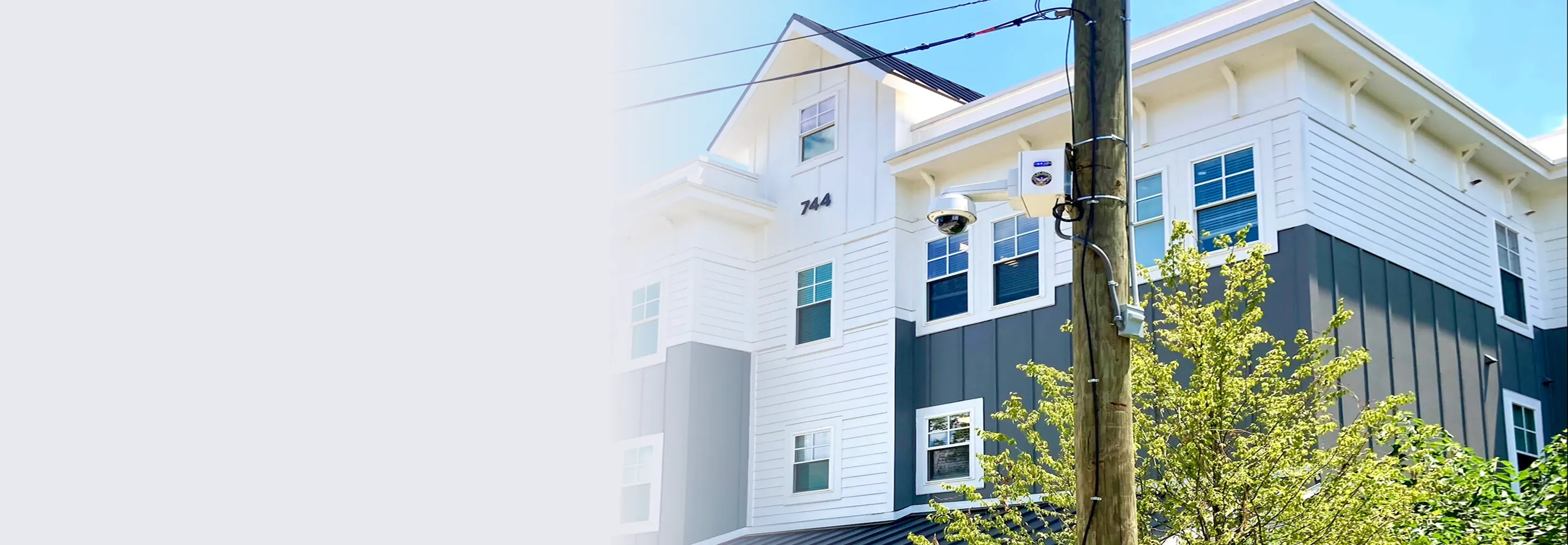 Modern multi-story residential building with gray and white siding and multiple windows under a clear blue sky.