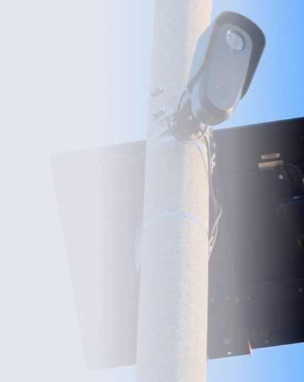 Security camera mounted on a tall pole with a blue sky background.