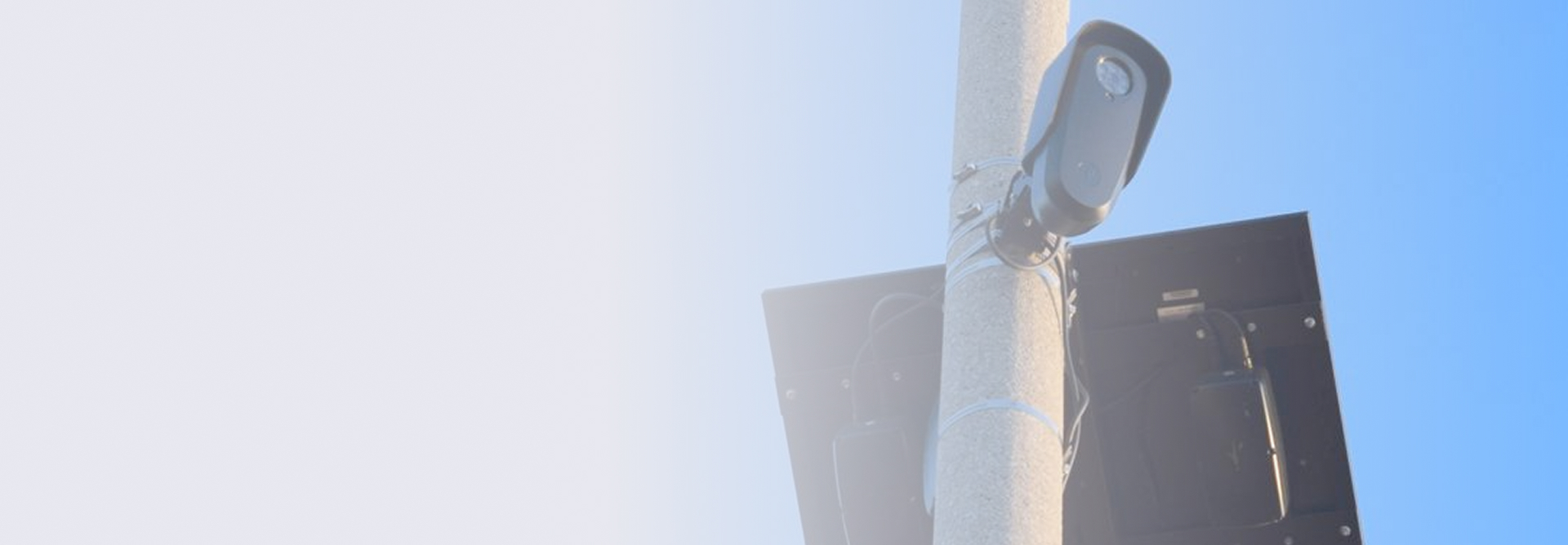 Security camera mounted on a pole with a solar panel attached, against a clear blue sky.