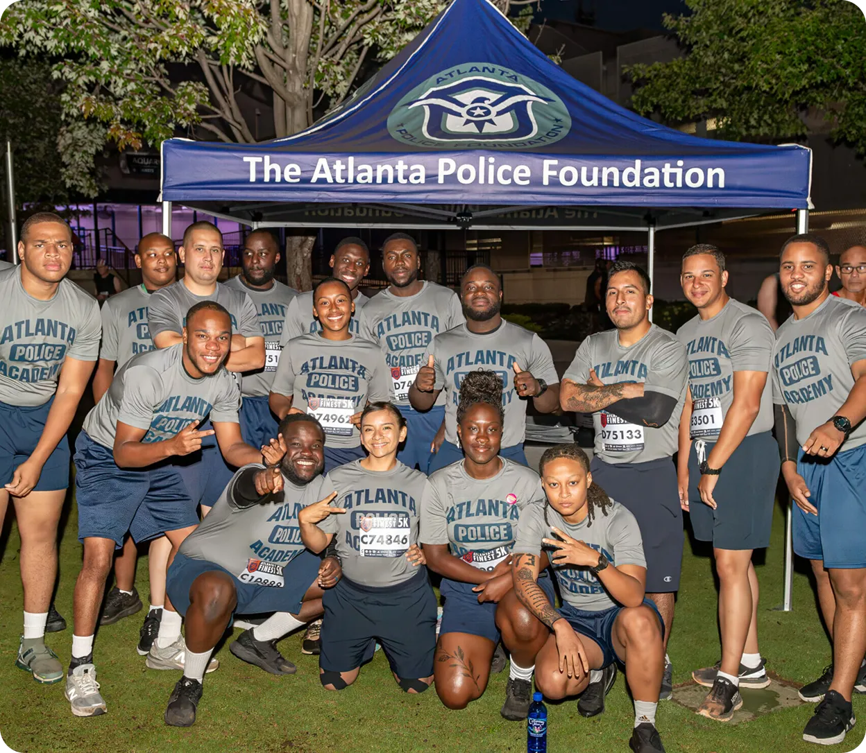 Group of Atlanta Police Academy participants posing and smiling under a tent labeled 'The Atlanta Police Foundation' at night.