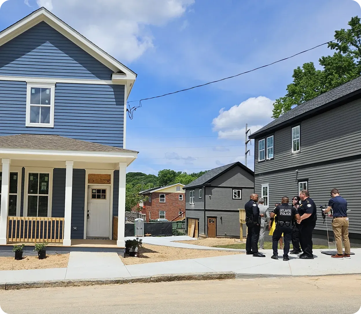 New residential neighborhood with several modern houses and a group of police officers speaking with a man on the sidewalk.