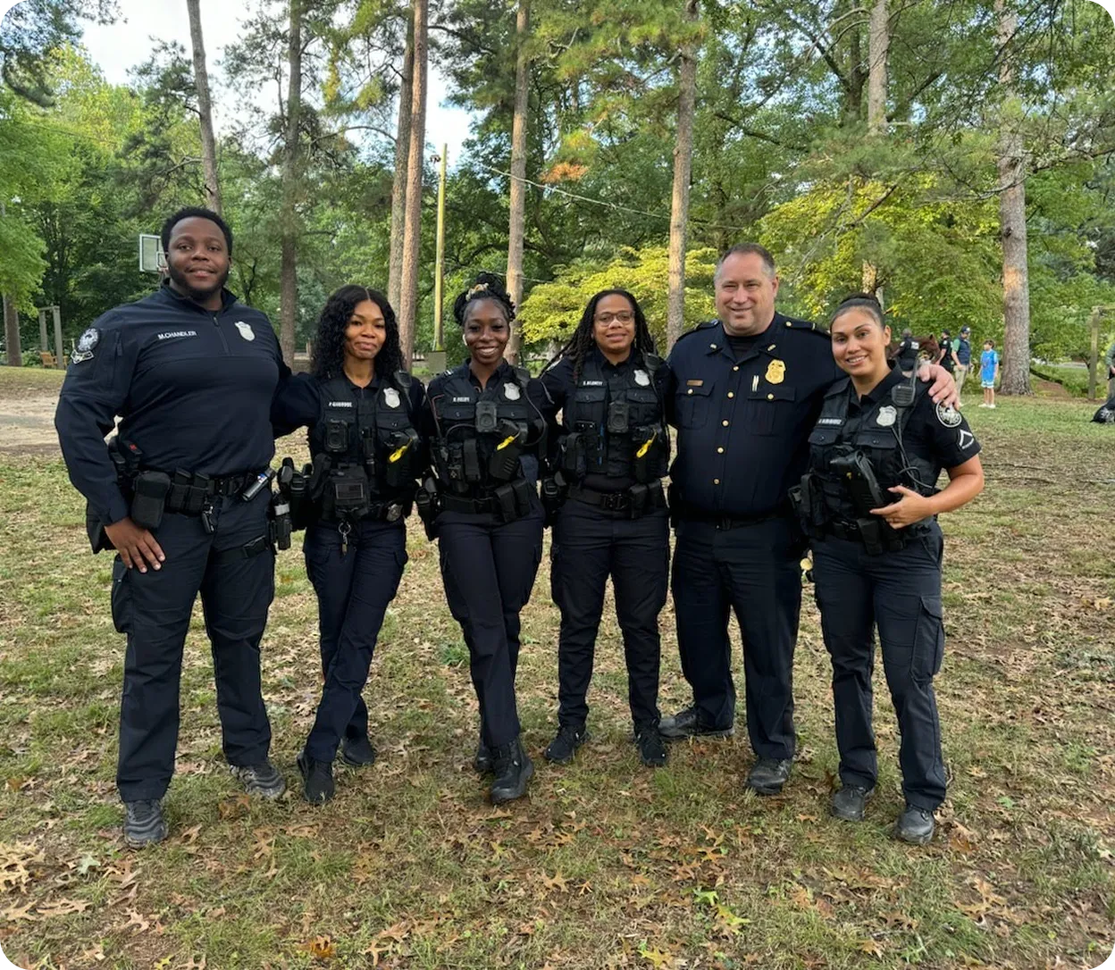 Six police officers standing arm in arm in a park with trees in the background.