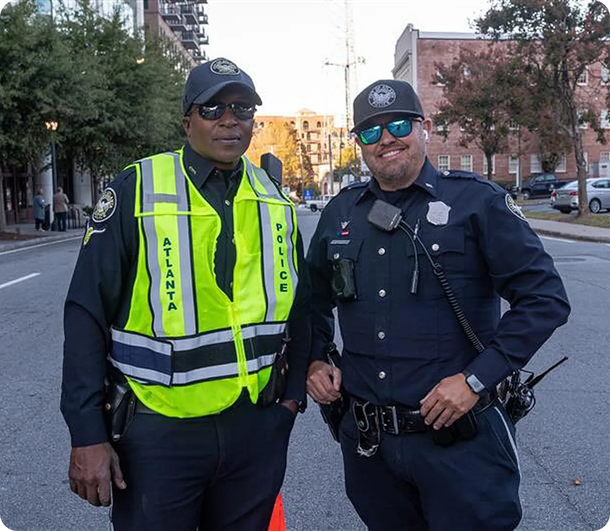 Two Atlanta police officers standing on a city street, one wearing a bright yellow reflective vest labeled 'Atlanta Police' and both wearing sunglasses and uniforms.