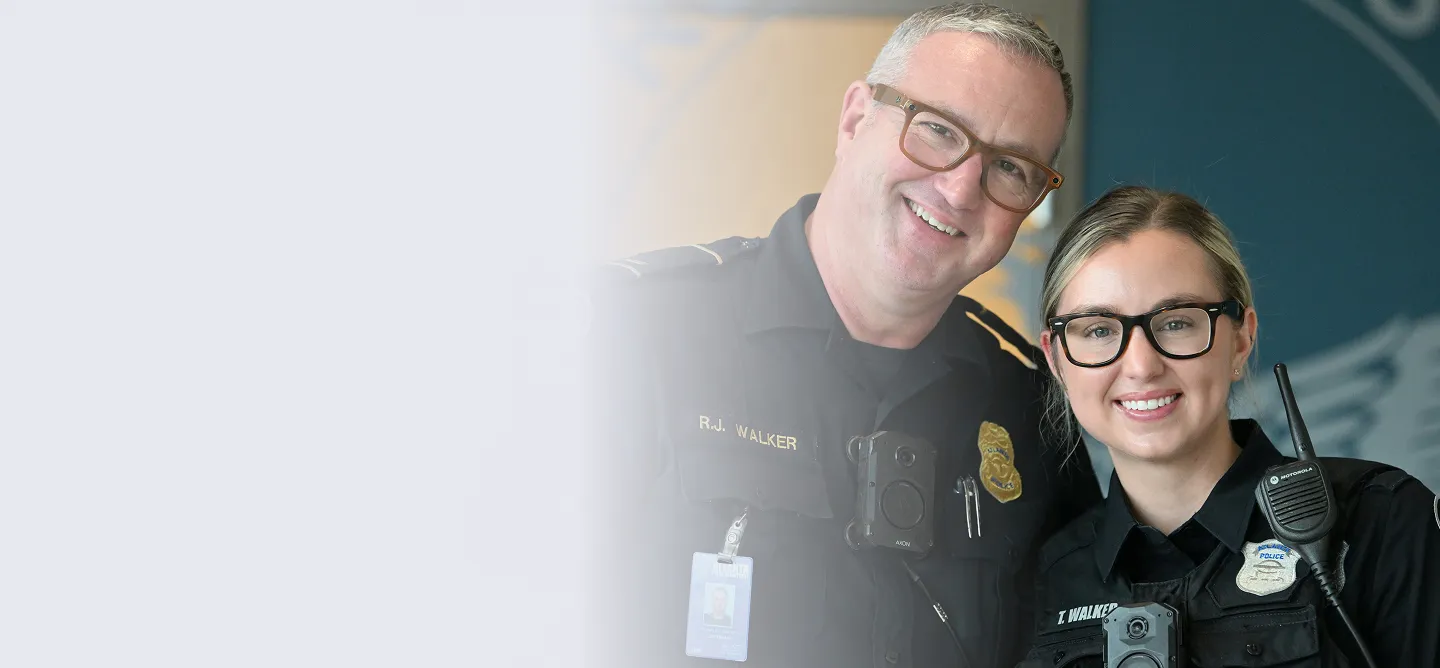 Two smiling police officers, a man and a woman, wearing black uniforms and glasses.