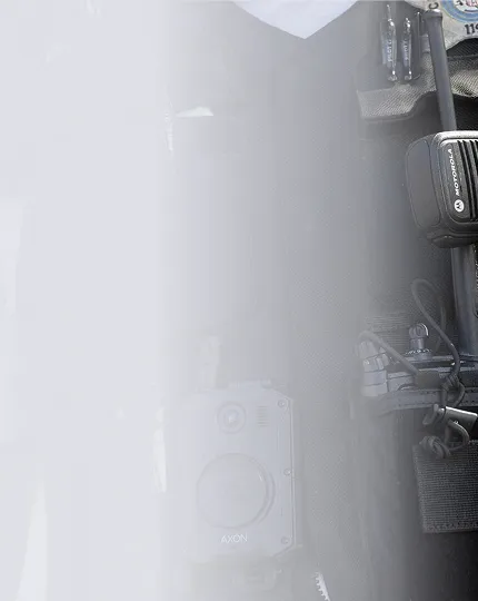 Close-up of Motorola radio and Axon body camera on a tactical vest or gear with pouches and straps.