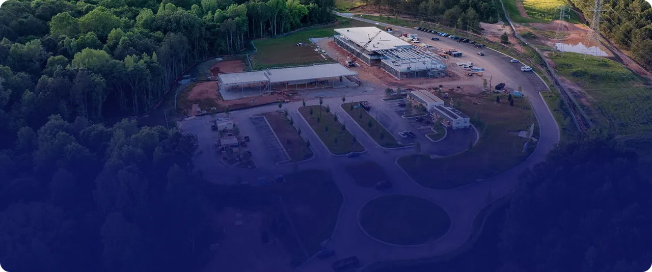 Aerial view of a construction site with multiple buildings in progress surrounded by trees and a circular driveway.