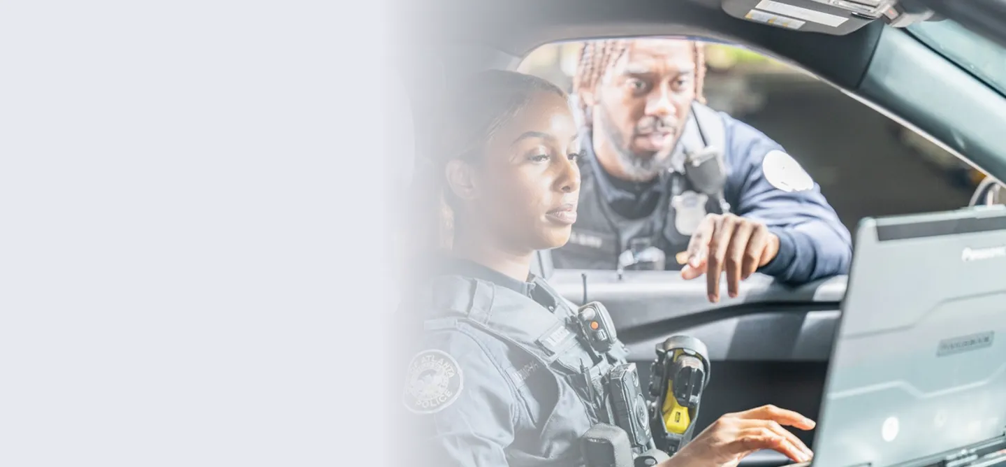 Two Atlanta police officers engaged in a discussion while working inside a police car, one focused on a laptop screen.