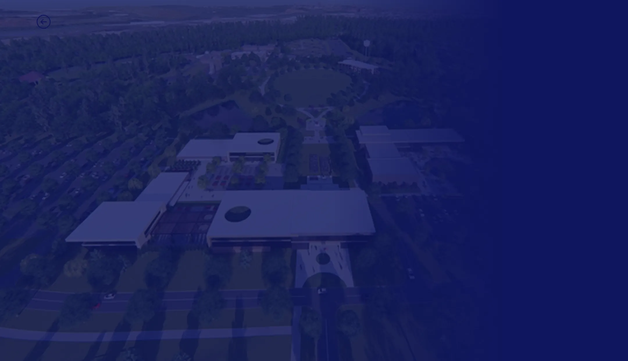 Aerial view of a modern campus or office complex with low-rise rectangular buildings, tree-lined walkways, large parking areas, and surrounding greenery.