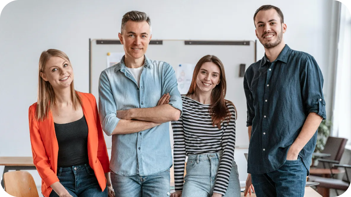 Vier junge Berufstätige stehen lächelnd in einem Büro mit einer Weißwandtafel im Hintergrund.