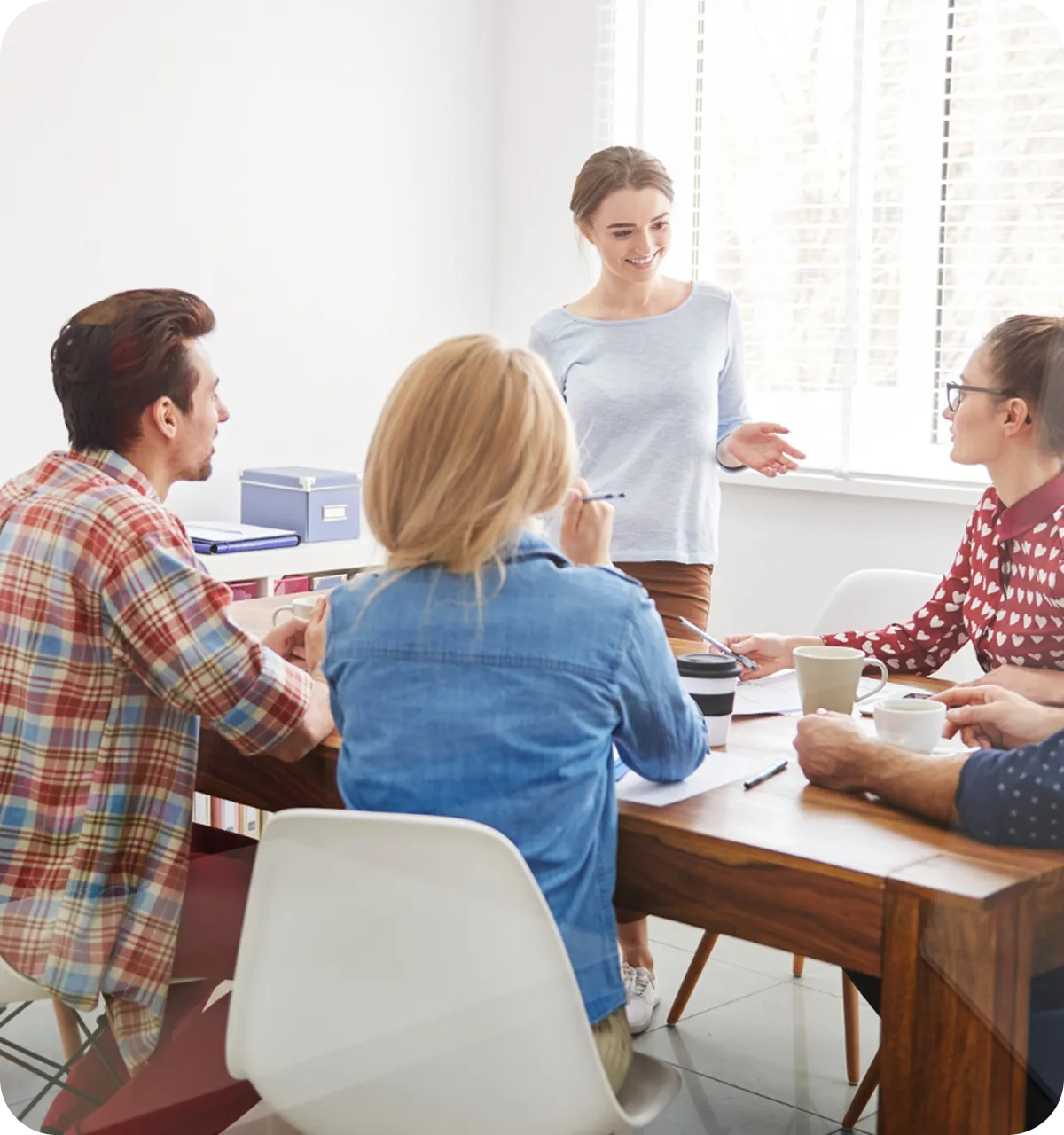 Gruppe von vier Personen, die bei Tageslicht in einem modernen Büro an einem Holztisch eine Diskussion führen.