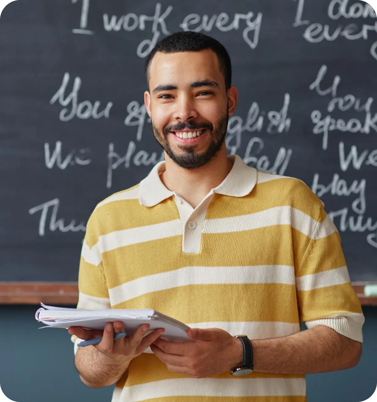 Junger Mann in gelb-weiß gestreiftem Poloshirt hält Notizblöcke und Stift vor einer Tafel mit englischen Sätzen.