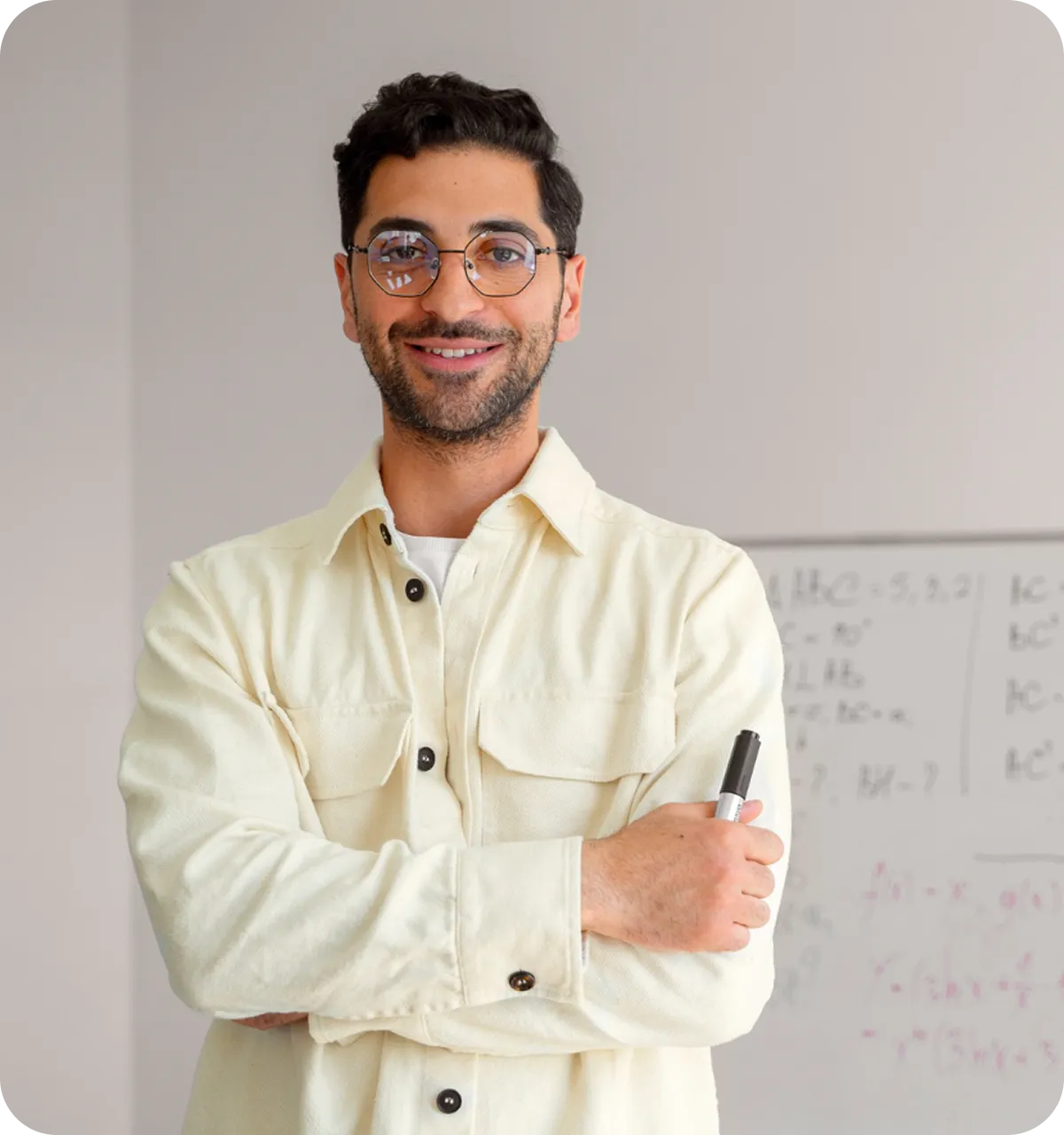 Lächelnder junger Mann mit Brille und hellem Hemd hält einen Marker vor einer Wandtafel mit mathematischen Formeln.