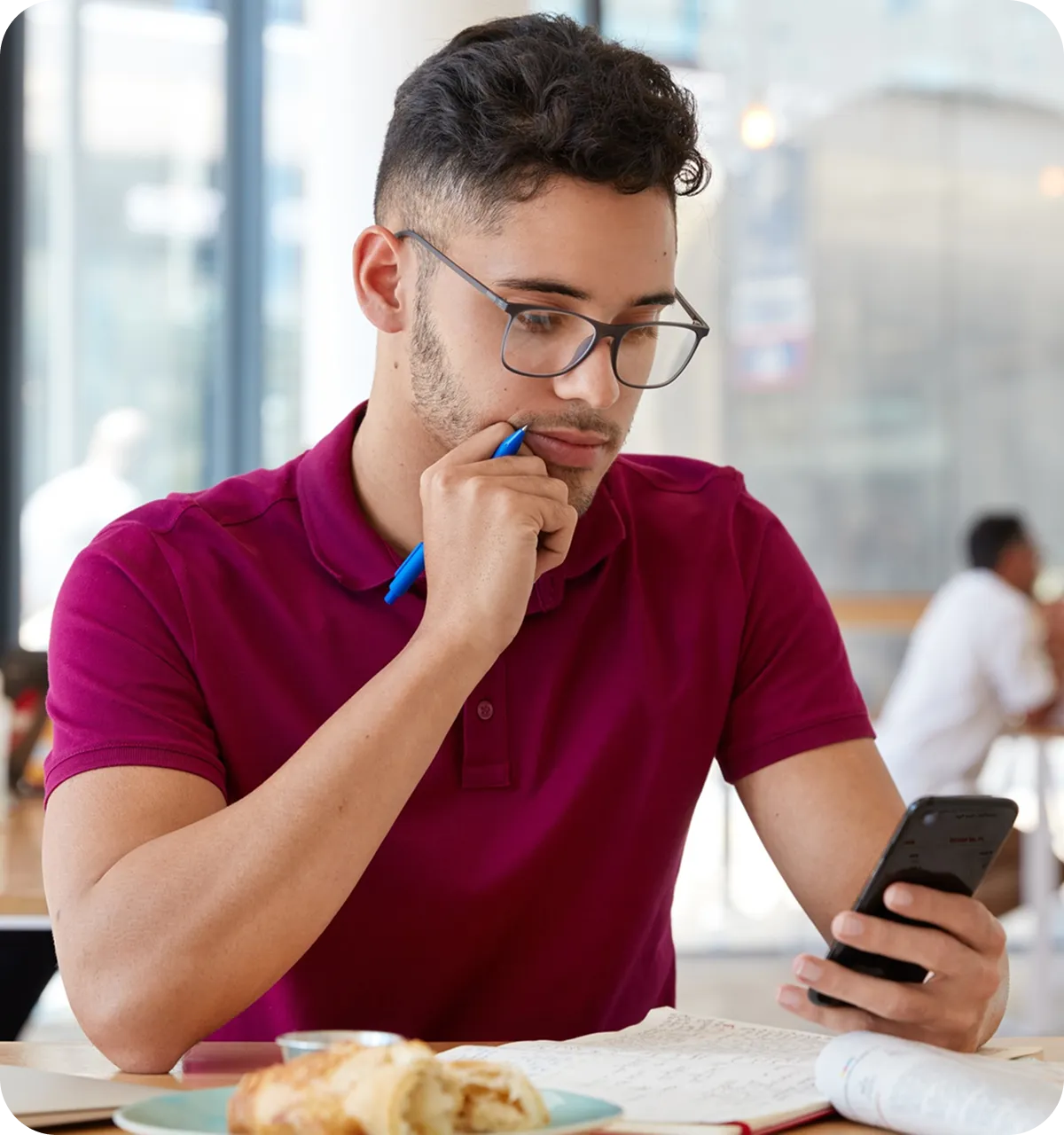 Junger Mann mit runder Brille liest konzentriert eine Nachricht auf ihrem Smartphone.