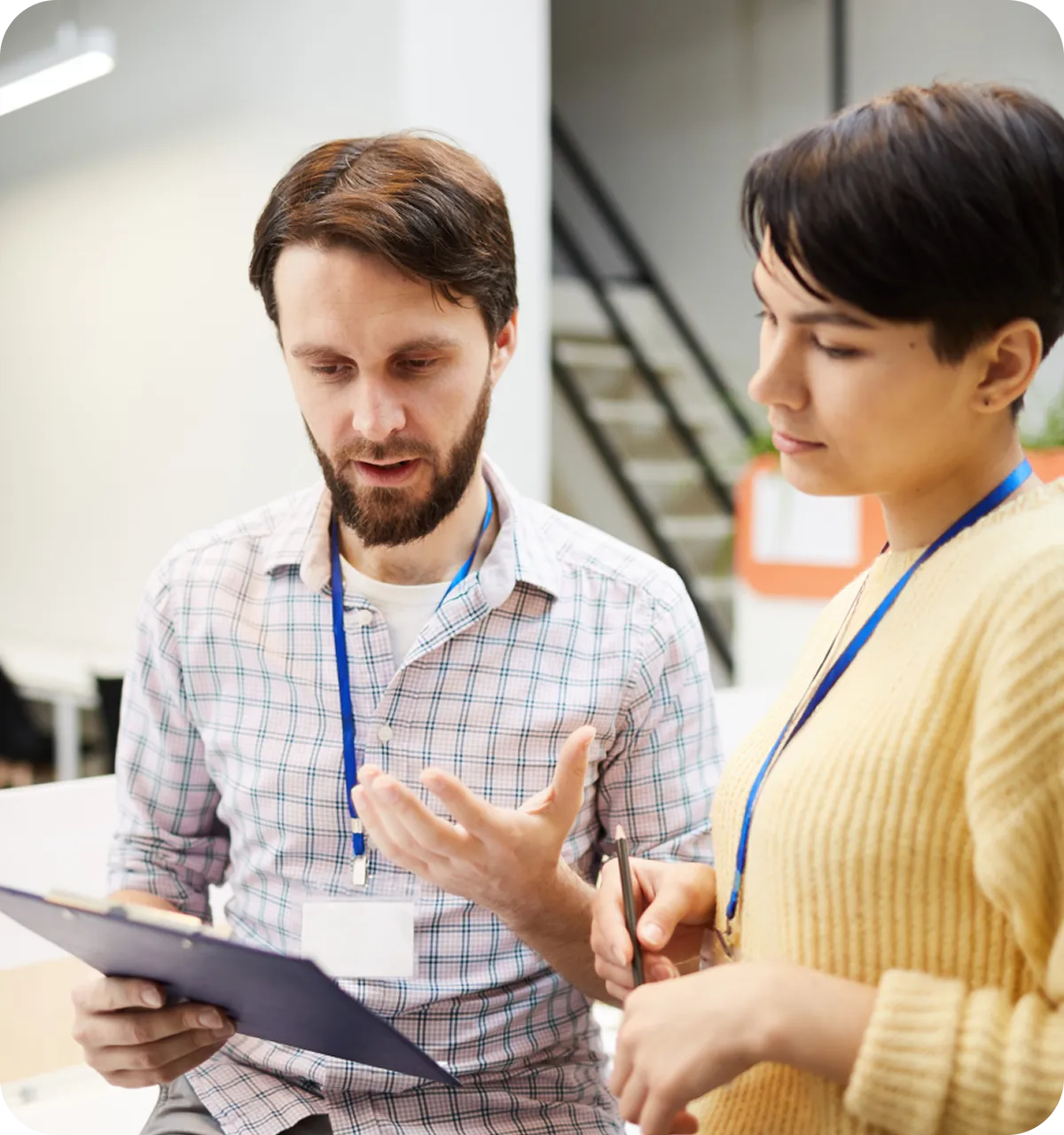 Ein besprechender Mann mit Klemmbrett erklärt einer Frau etwas, die aufmerksam zuhört und einen Stift hält.