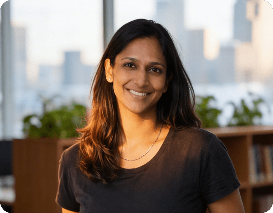 A smiling woman with dark hair in a casual black top, posing in front of a brightly lit office window.