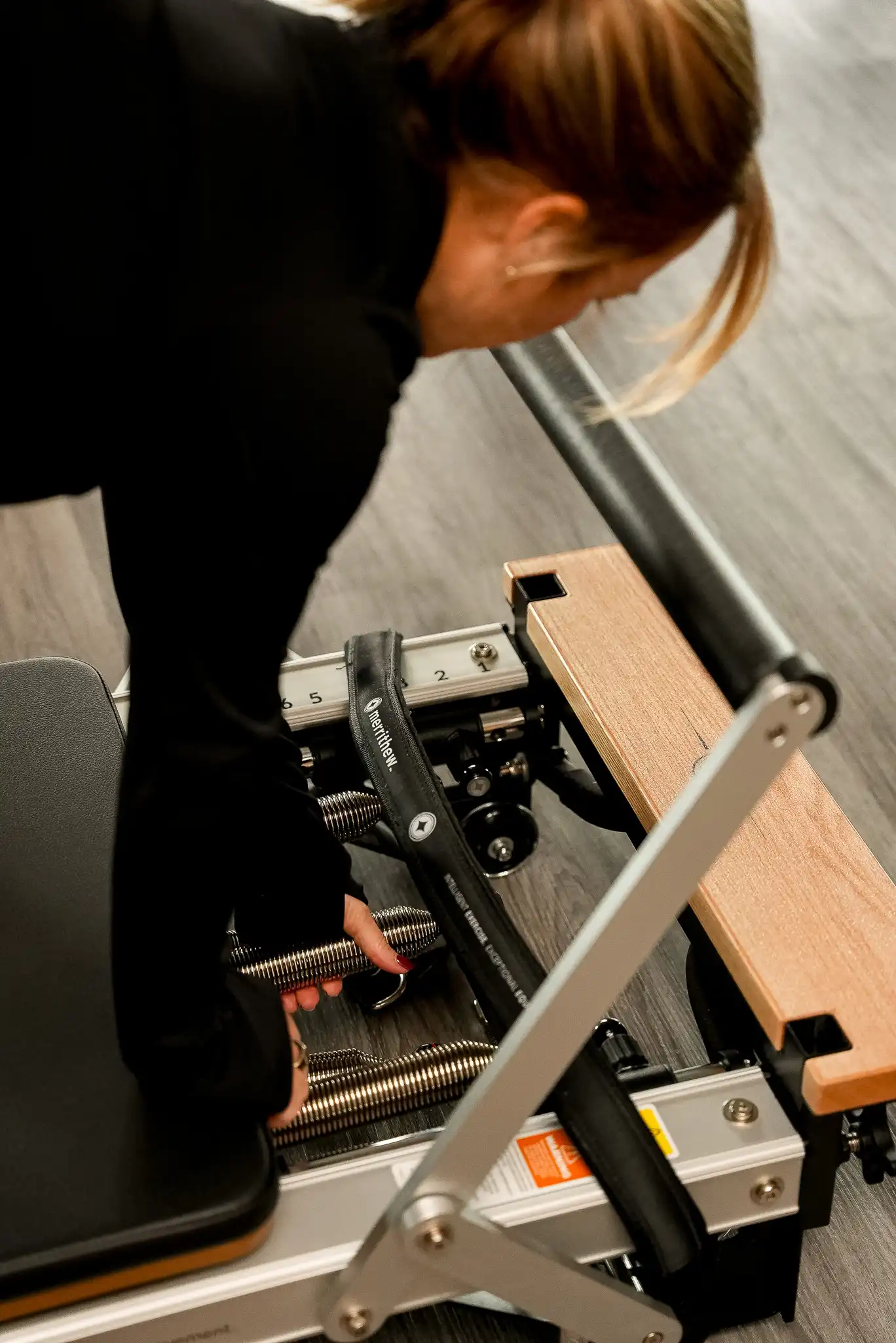 Vue plongeante sur une instructrice en noir réglant les ressorts d’un reformer Merrithew au Studio KŌR.