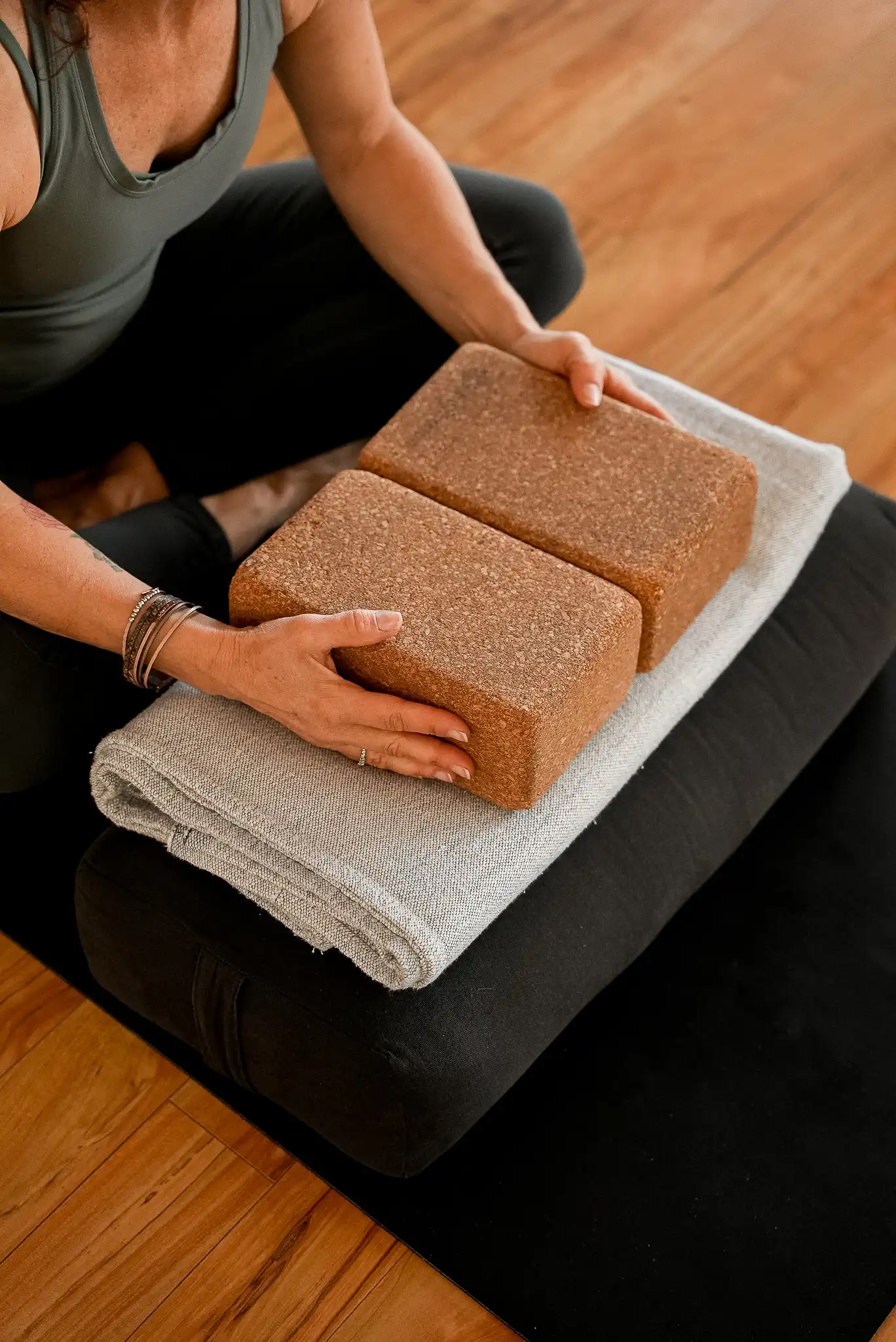 Mains posées sur deux blocs de yoga en liège, personne assise en tailleur sur un bolster de yoga.