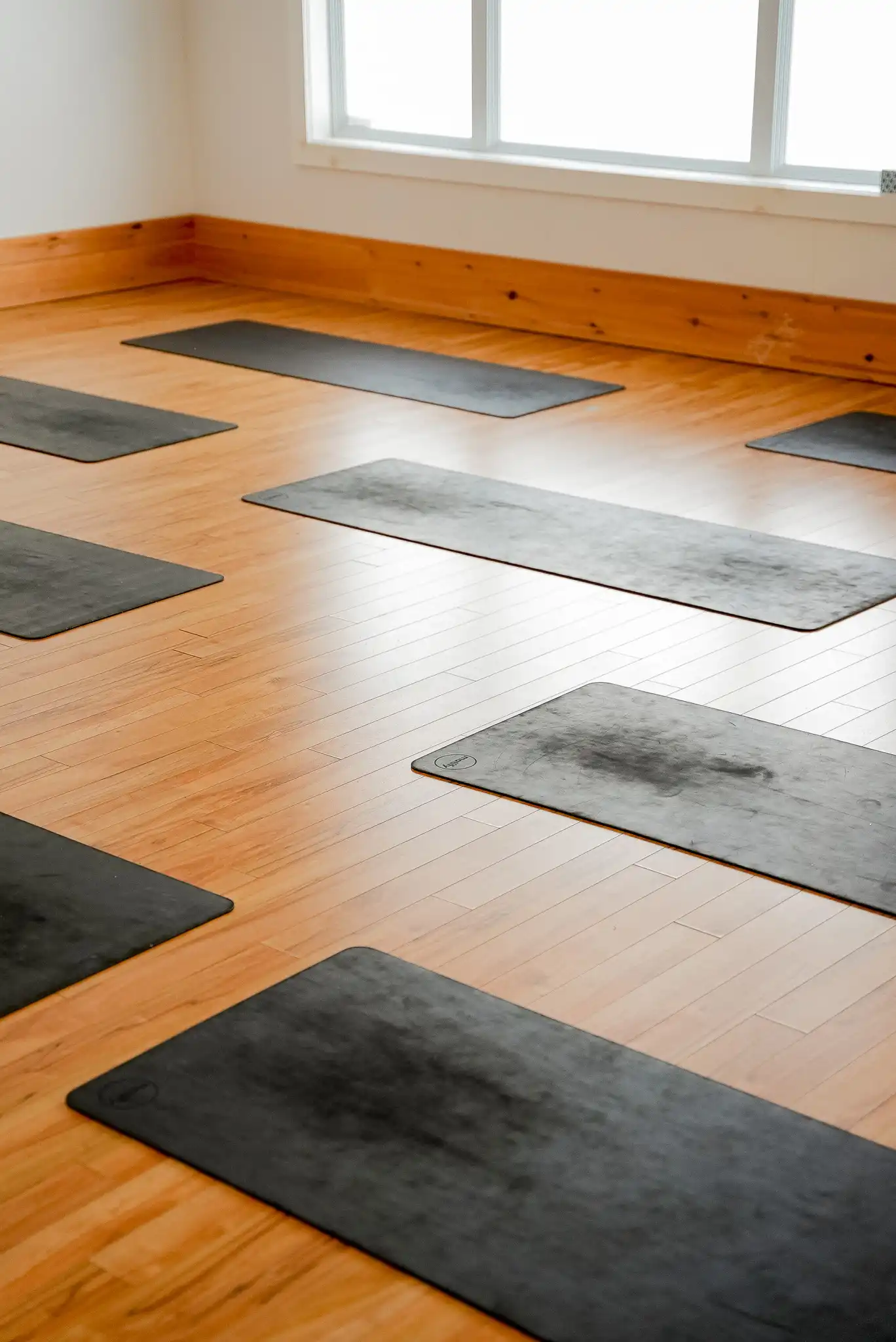Salle de yoga Studio KŌR avec huit tapis gris disposés sur un plancher de bois franc, lumière naturelle.