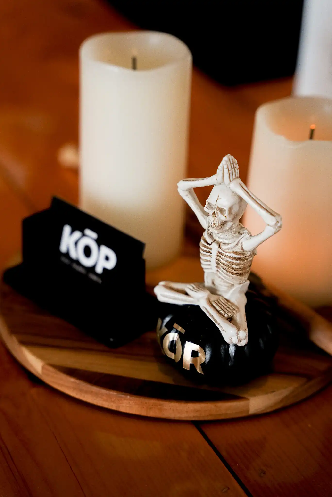 Statuette squelette en pose de yoga sur un objet KŌR noir, entourée de bougies blanches et d'une carte de visite Studio KŌR.