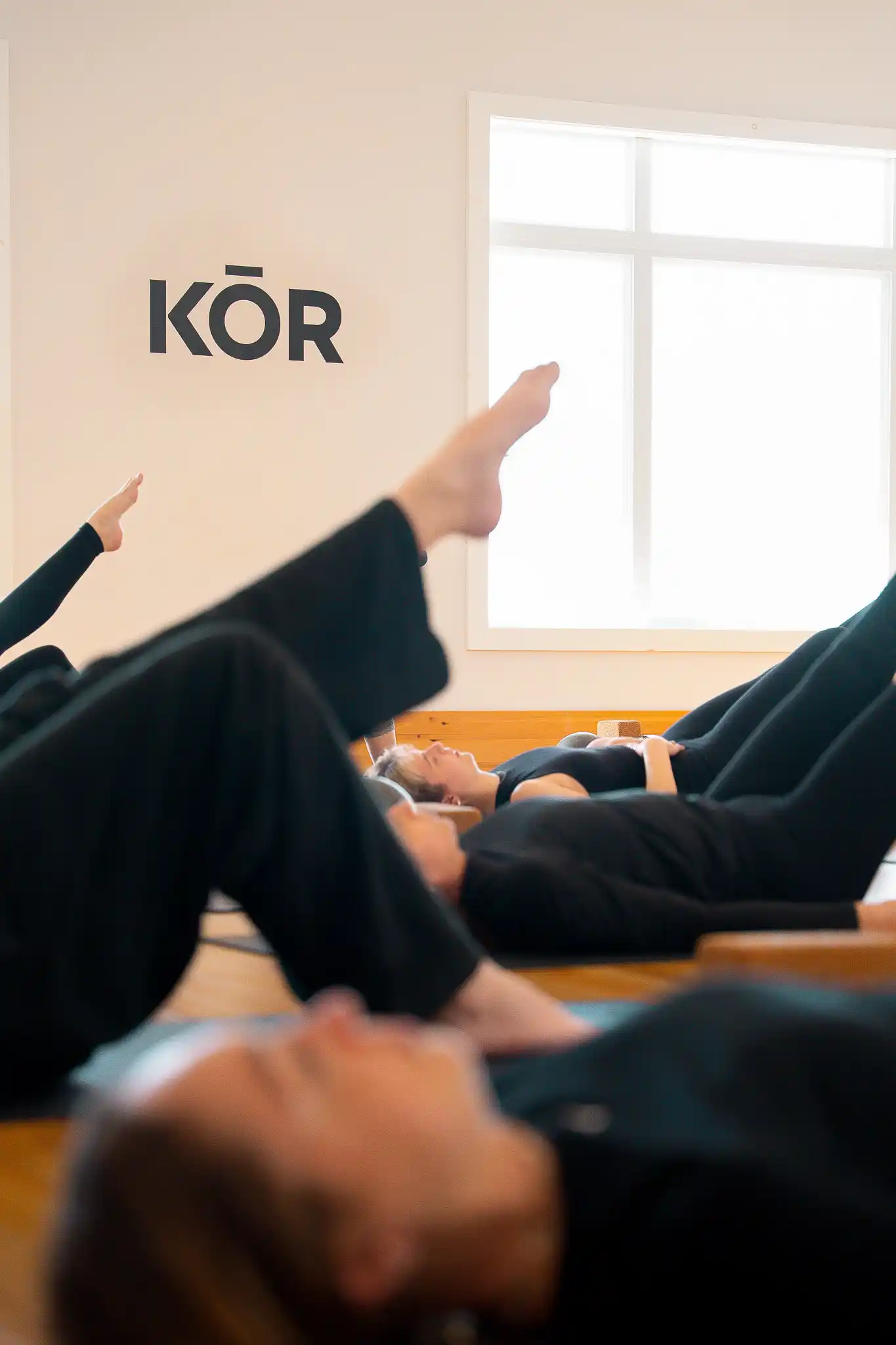 Participants allongés au sol, jambes vers le ciel, pendant un cours de Pilates au Studio KŌR.