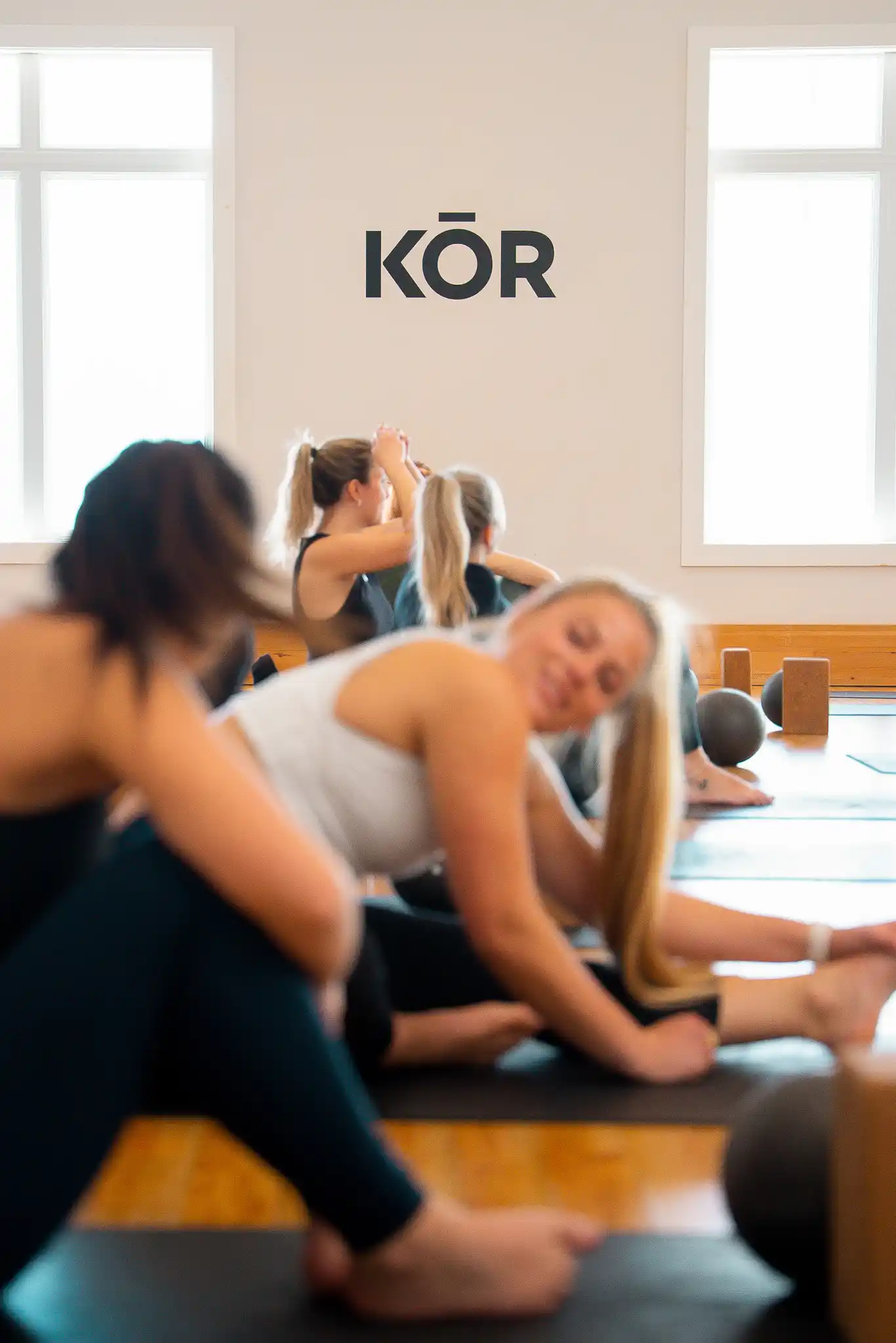 Cours collectif au sol au Studio KŌR, participantes en flexion avant sous le logo KŌR.