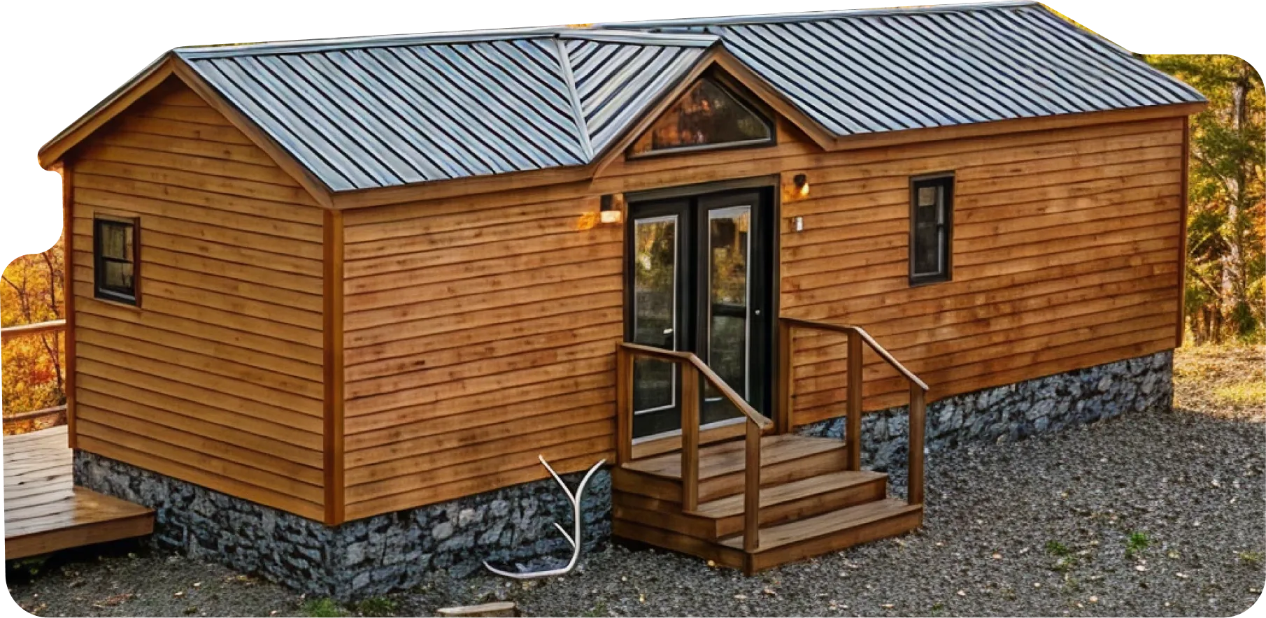 Single-story wooden cabin with stone foundation, metal roof, small front porch, and surrounded by autumn trees.