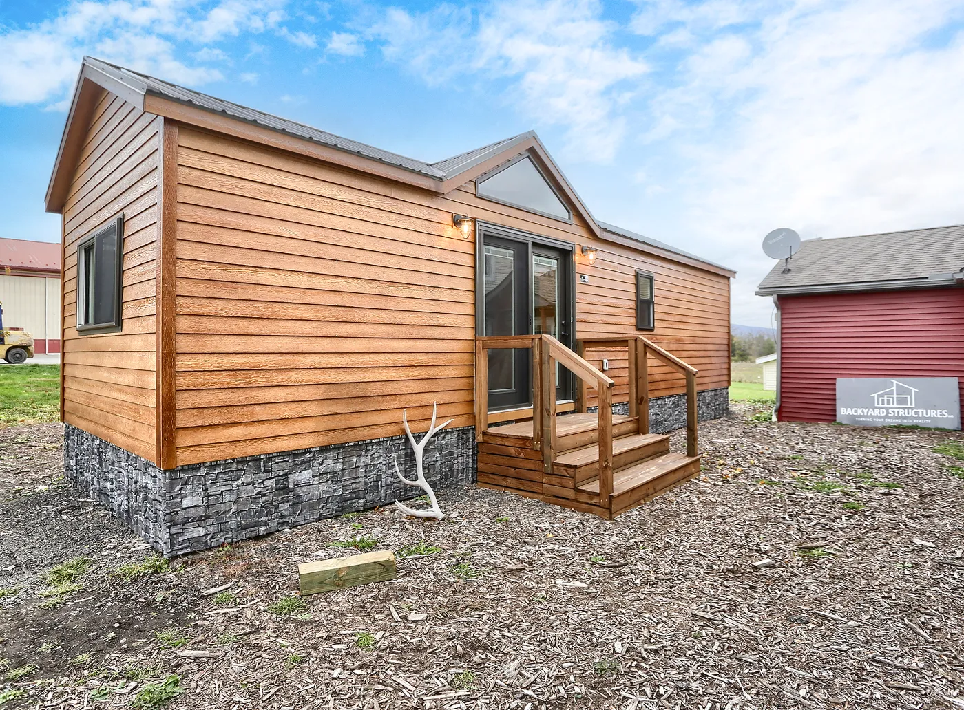 Forest Glen cabin with stone foundation, two outdoor lights, a small porch with steps, and a glass front door under a triangular window.