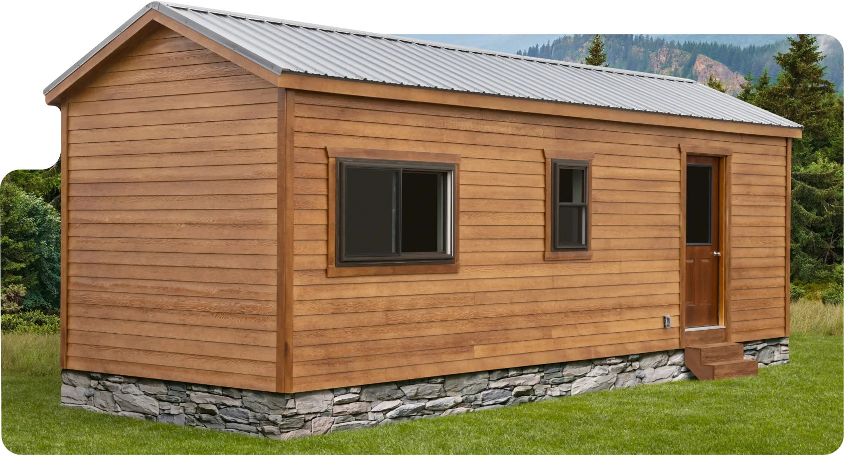 Small wooden cabin with stone foundation on green grass, surrounded by pine trees and misty mountains in the background.