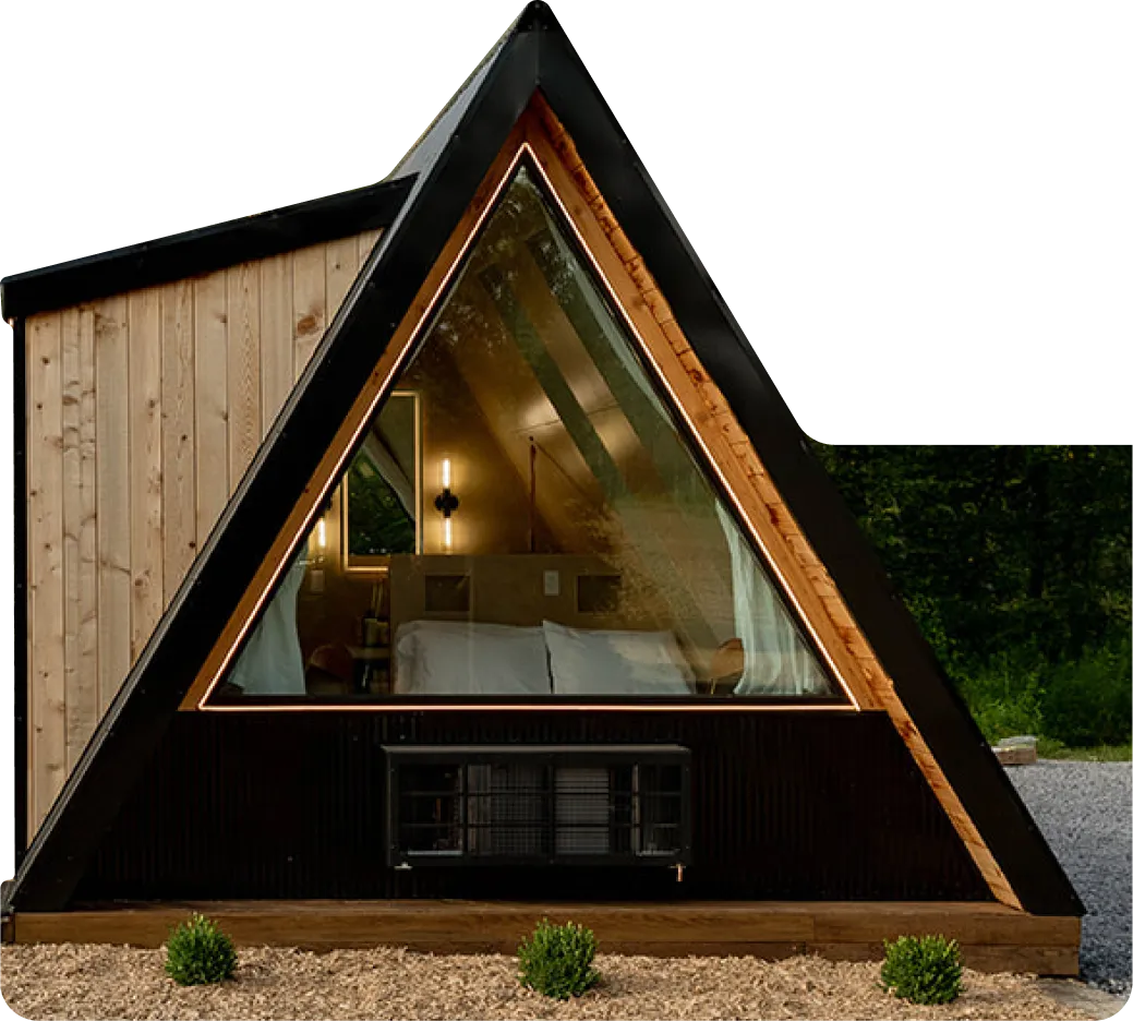 Modern A-frame cabin with a large triangular front window showing a cozy bed inside.