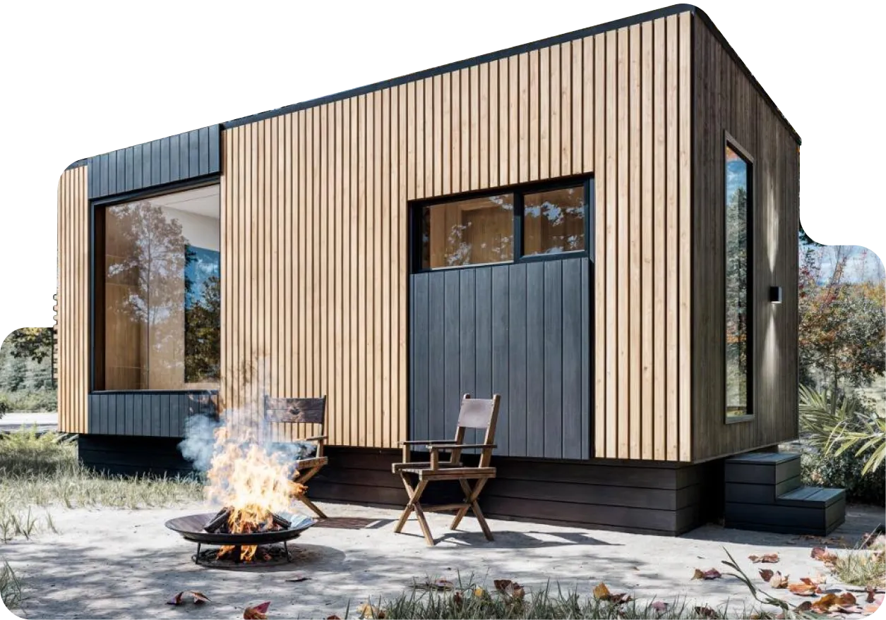 A modern cabin model Vista, with vertical wood siding, large windows, and two chairs beside a fire pit in an outdoor setting.