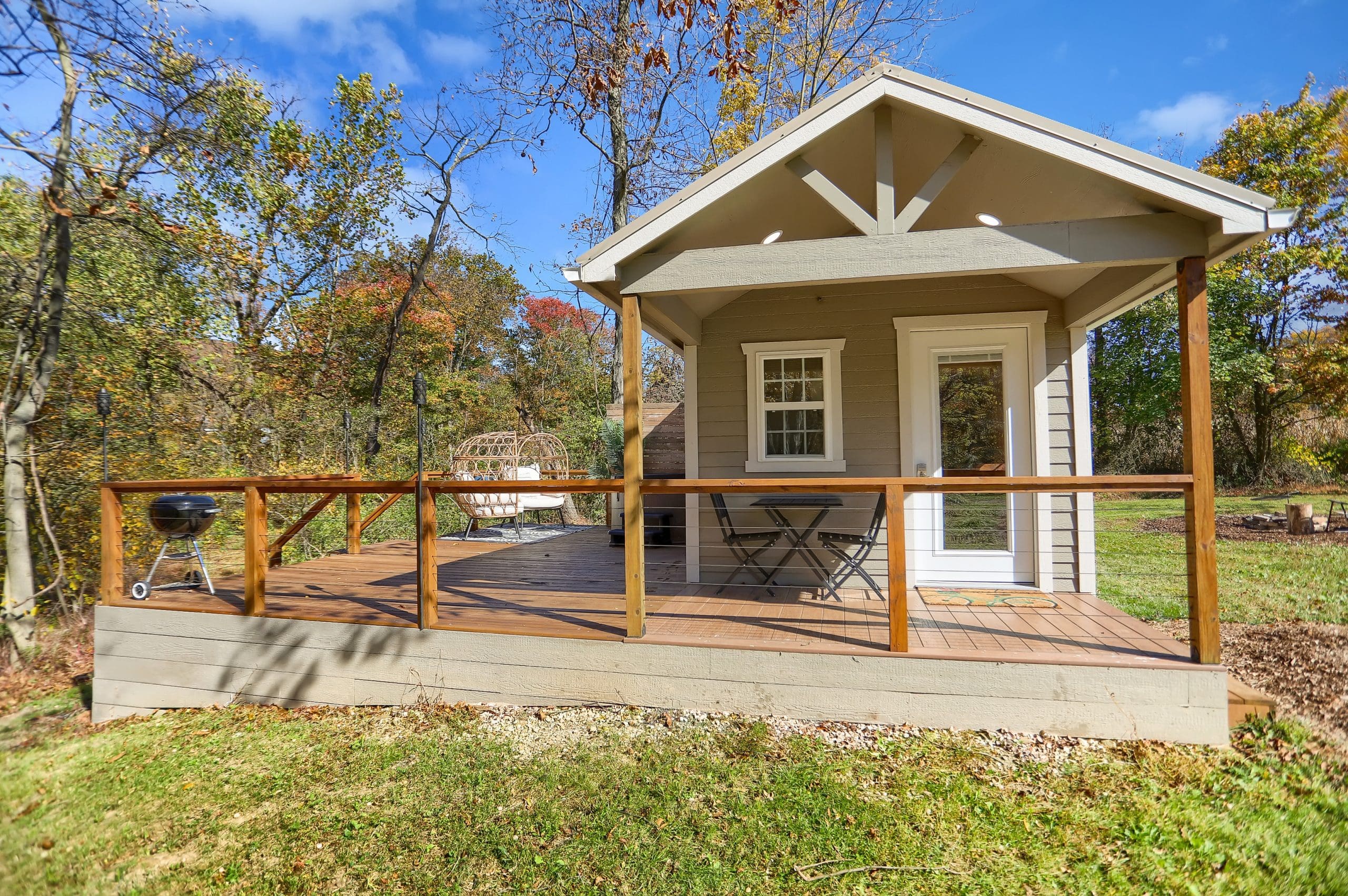 a small cabin out in nature, with a porch and a grill on the porch