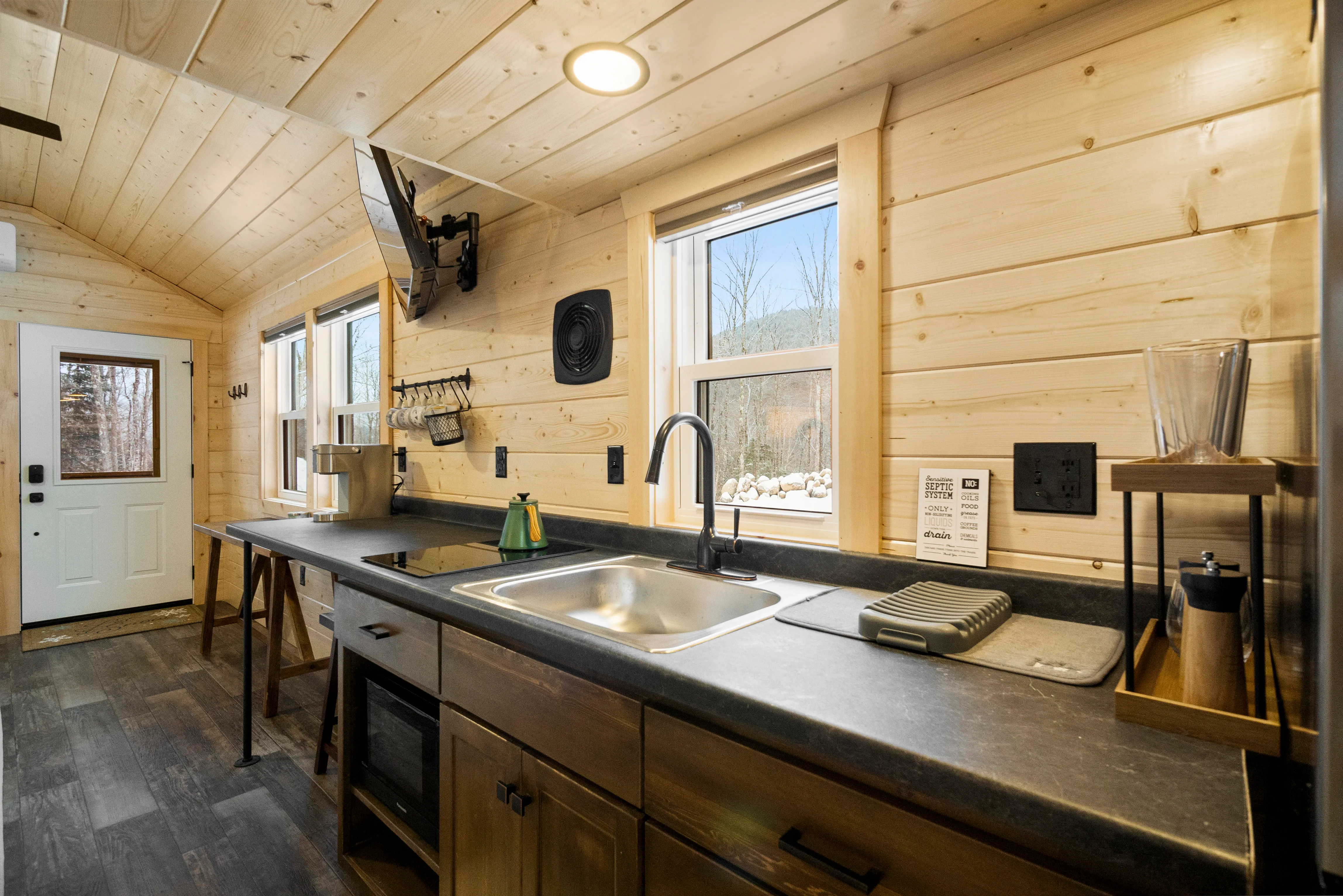 A modern kitchen with wood-paneled walls and ceiling, a countertop with a sink, windows.