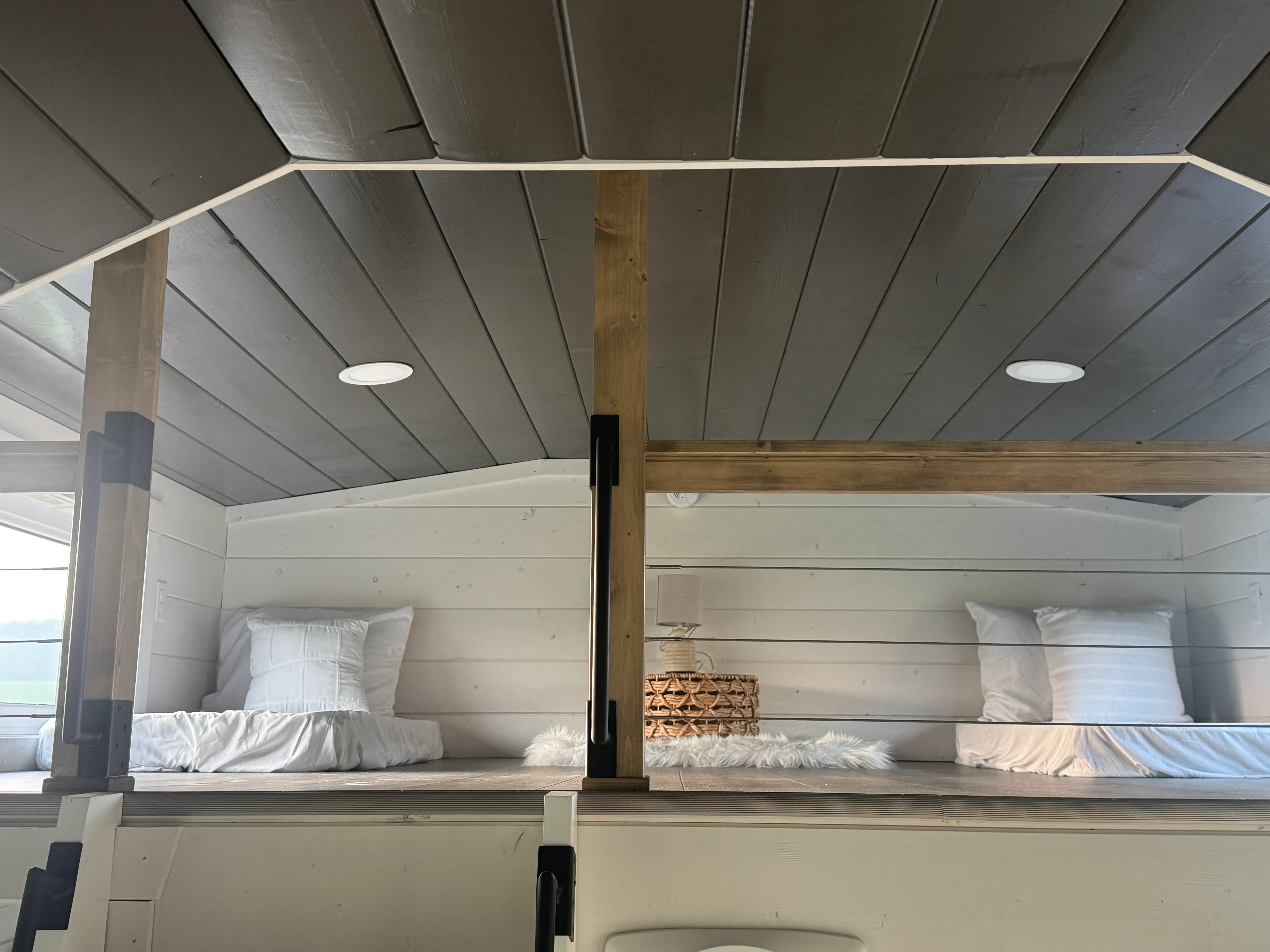 A lofted space with two twin beds, each bed with white bedding and pillows, and a small nightstand with a lamp in between.