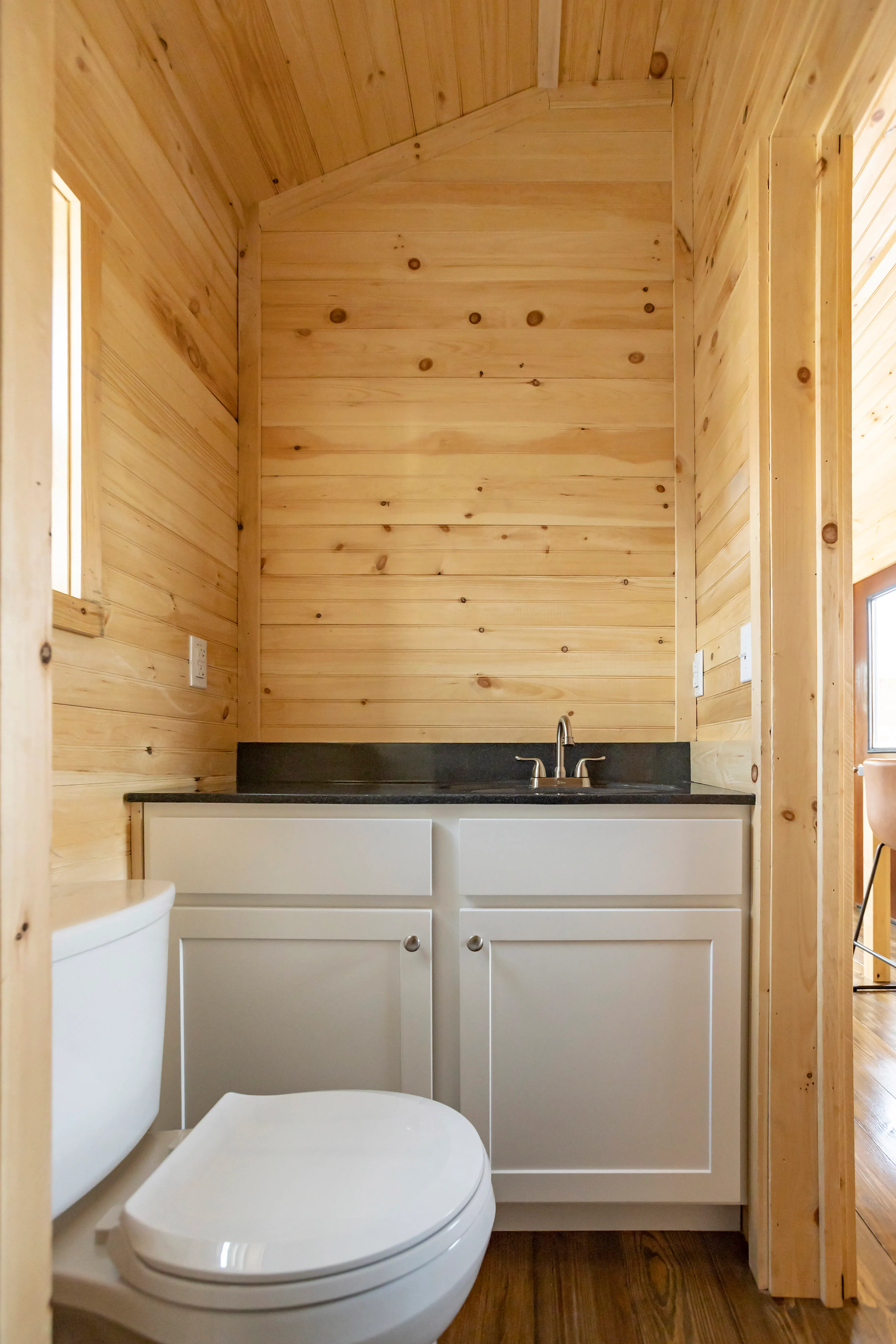 A small bathroom with wood-paneled walls, white vanity with a sink and faucet, white toilet, and a dark countertop.